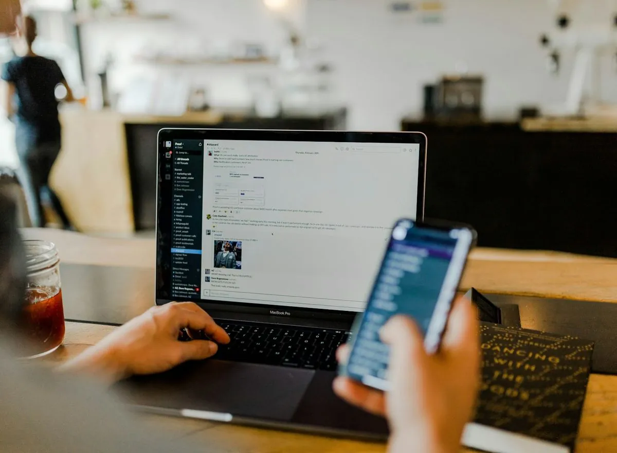 Person using a smartphone beside an open laptop.
